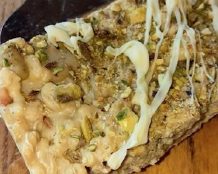 Piece of dessert topped with nuts and a creamy layer on a wooden surface.