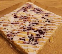 A rectangular pastry topped with icing and scattered almond flakes.