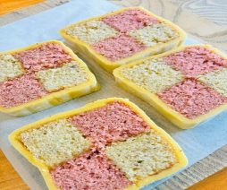 Four checkerboard cake slices with pink and yellow sections on a white background.